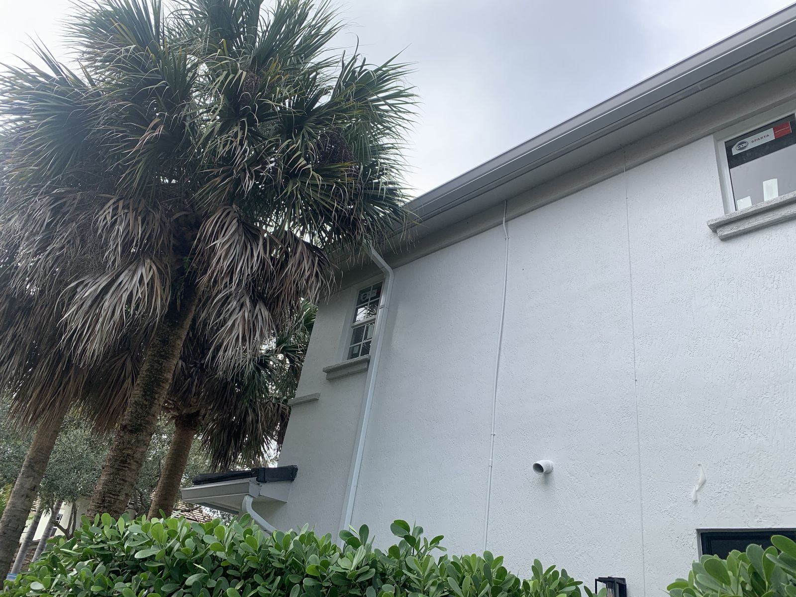 White aluminum downspout carrying rainwater down the exterior wall of a Florida home