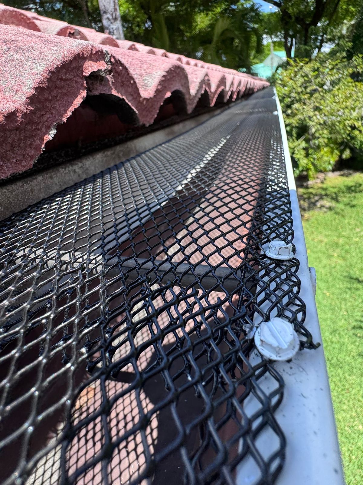 Black mesh gutter guard installed over a barrel-tile roof edge to keep leaves out