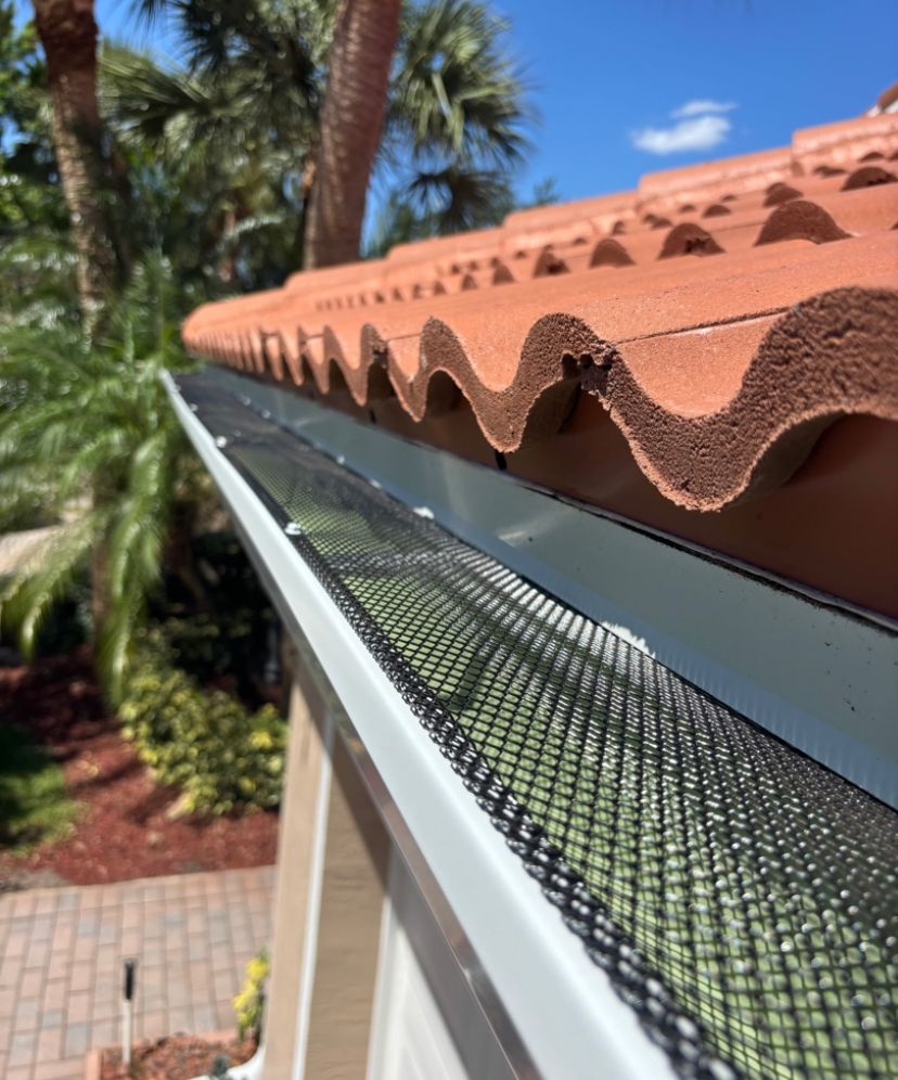 Black mesh leaf guard protecting a gutter beneath a barrel-tile roof