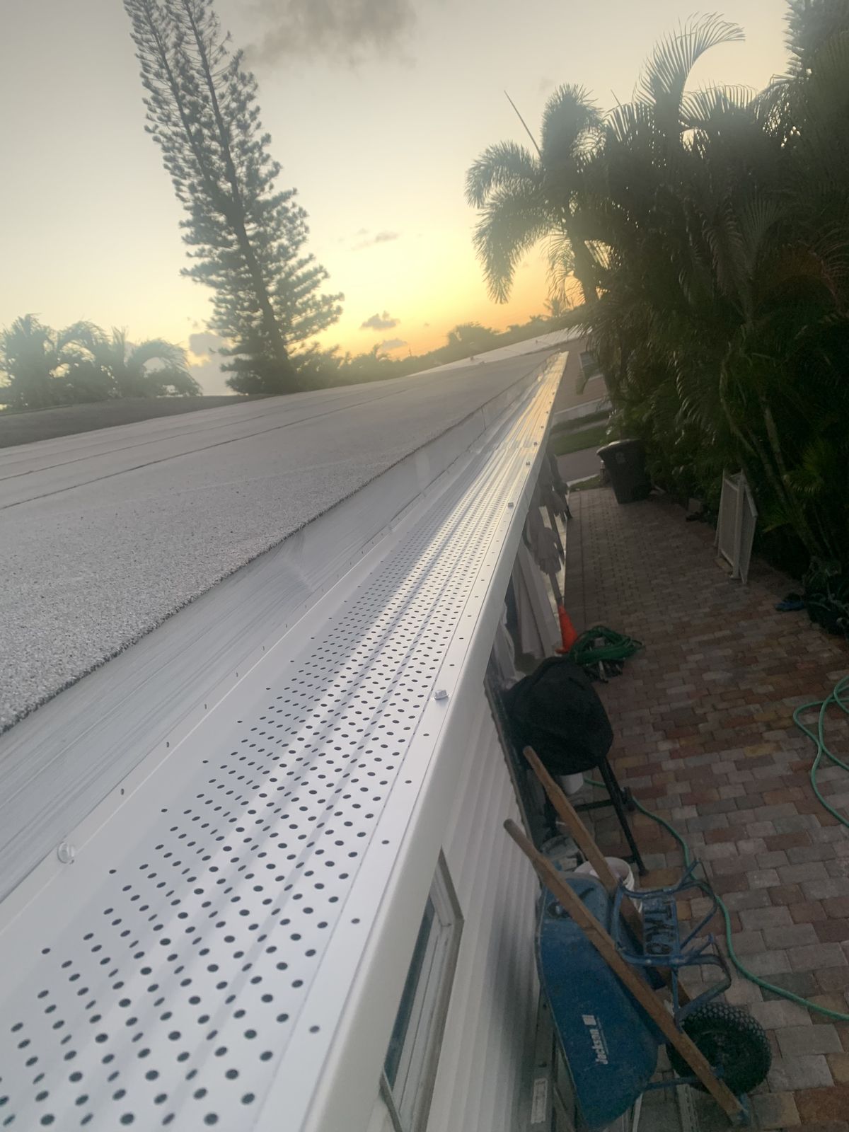 Perforated aluminum leaf guard running along a seamless gutter at dusk